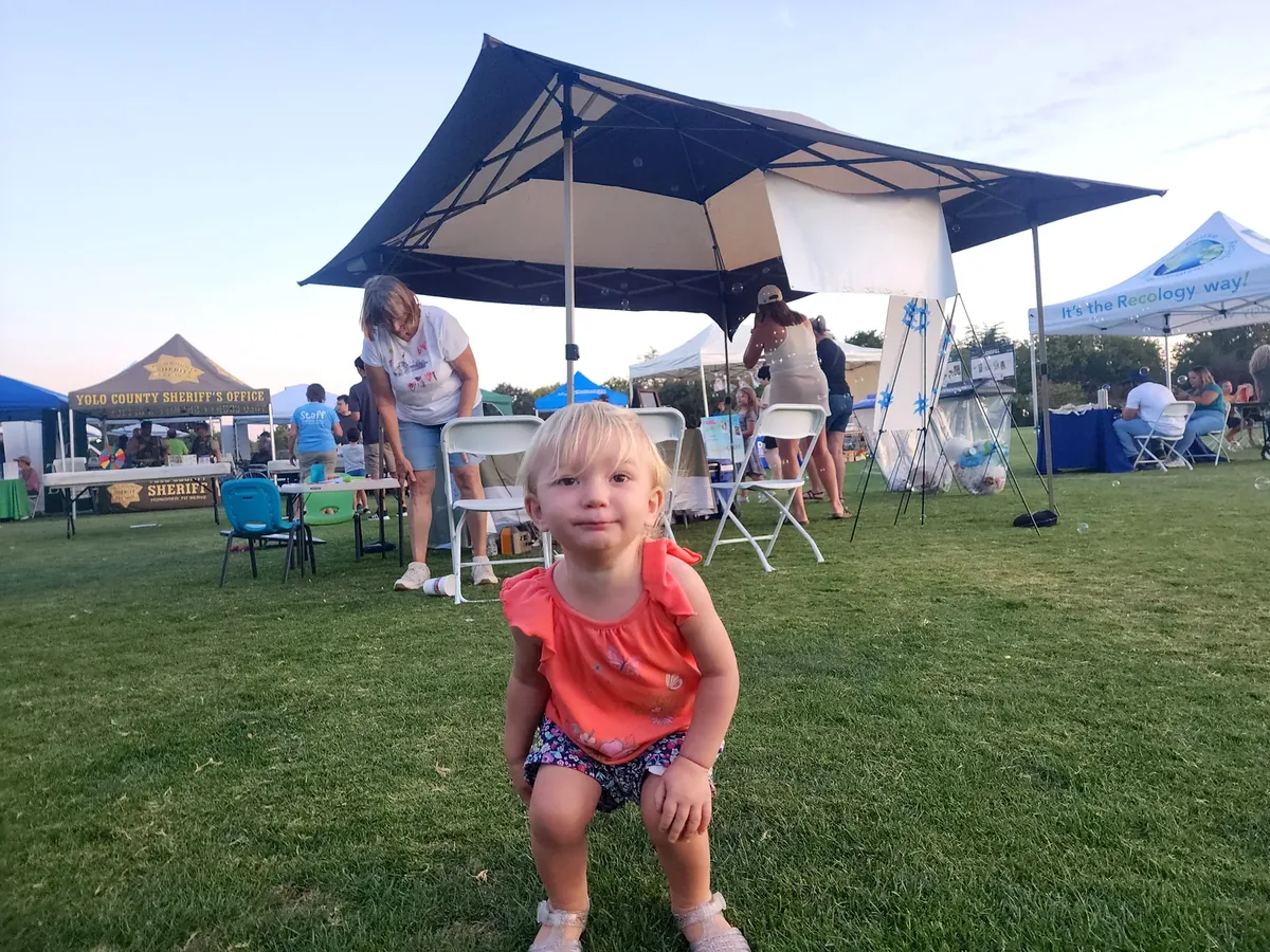 A young Davis child smiling in golden evening light at a Family Fun Fest booth